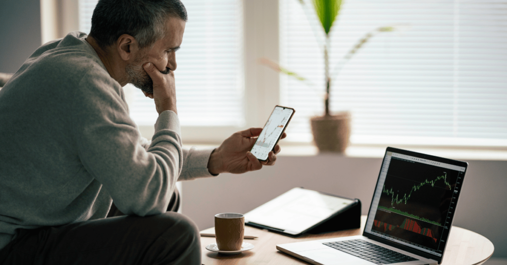 A man looking puzzled while looking at both his laptop and phone screen.